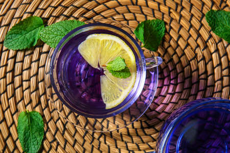 Glass cup of organic butterfly tea with lemon and mint on table, closeup