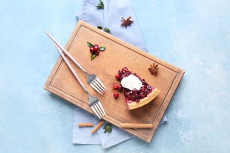 Board with piece of tasty lingonberry pie and spices on color background