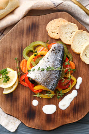 Wooden board of tasty sea bass fish with vegetables on tableの写真素材