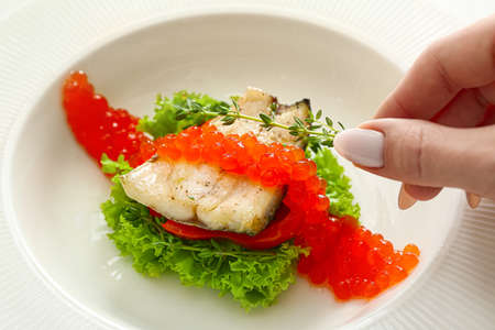 Woman decorating plate of tasty sea bass fish with thyme, closeupの写真素材