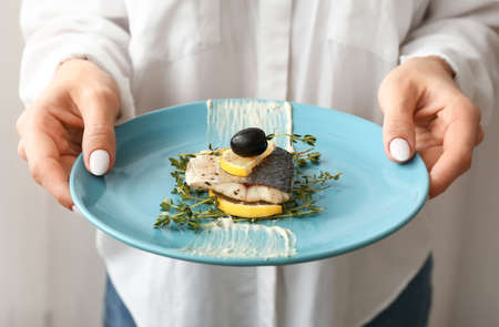 Woman holding plate of tasty sea bass fish on light background, closeupの写真素材