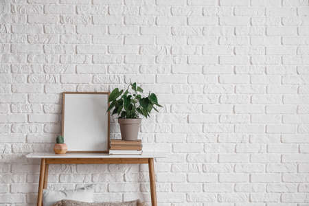 Beautiful houseplant and blank frame on table near white brick wallの写真素材