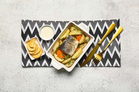 Baking dish of tasty sea bass fish with vegetables on light backgroundの写真素材
