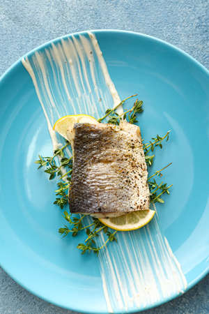 Plate of tasty sea bass fish on blue background