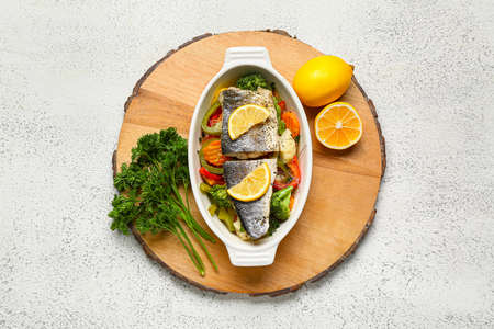baking dish of tasty sea bass fish with vegetables on light backgroundの写真素材