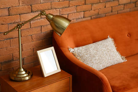 Golden lamp with picture on wooden table and sofa near brick wall