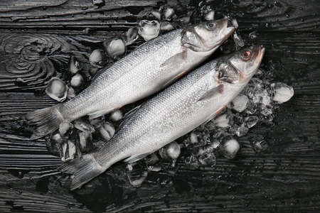 Fresh uncooked sea bass fish on black wooden background