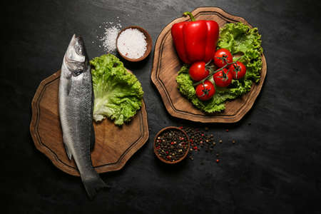 Wooden boards with fresh uncooked sea bass fish and vegetables on black backgroundの写真素材