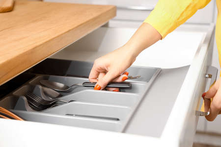 Woman taking spoon from drawer in kitchen, closeup