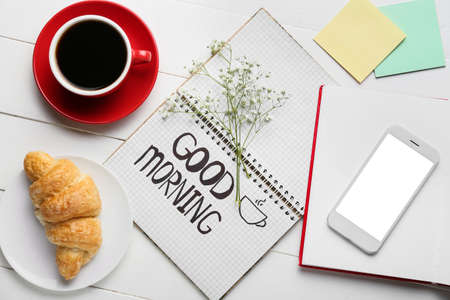Composition with cup of coffee, croissant, mobile phone and stationery on light wooden backgroundの写真素材
