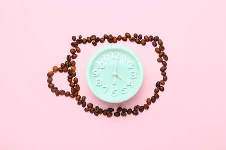 Cup made of coffee beans and alarm clock on pink backgroundの写真素材