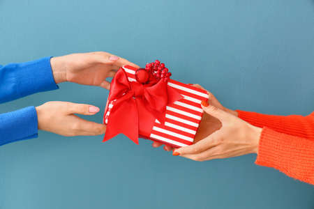 Female hands with Christmas gift on color background