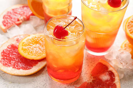 Glasses of tasty Tequila Sunrise cocktail with fresh fruits on white backgroundの写真素材