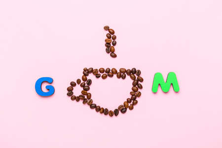 Color letters GM and cup made of coffee beans on pink background