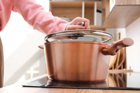 Woman putting lid on copper cooking pot in kitchen, closeup