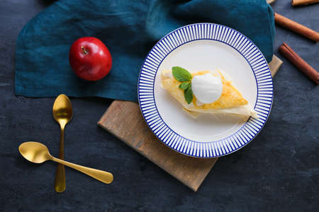 Plate with piece of tasty apple strudel on black background