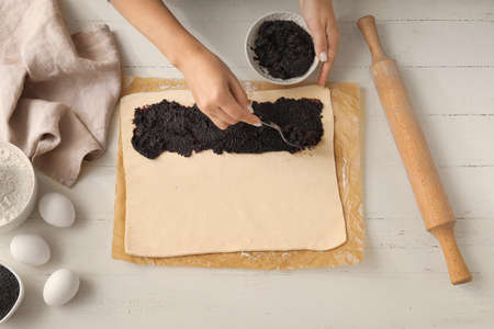 Woman preparing tasty poppy seed strudel on light wooden backgroundの写真素材