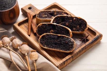 Board with pieces of tasty poppy seed strudel on white wooden background