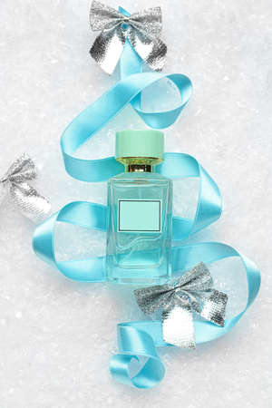 Composition with bottle of perfume, ribbon and Christmas bows on snow background