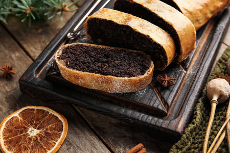 Board with tasty poppy seed strudel on wooden background, closeup