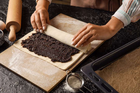 Woman preparing tasty poppy seed strudel at kitchen table