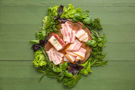 Board with uncooked and smoked bacon on green wooden backgroundの写真素材