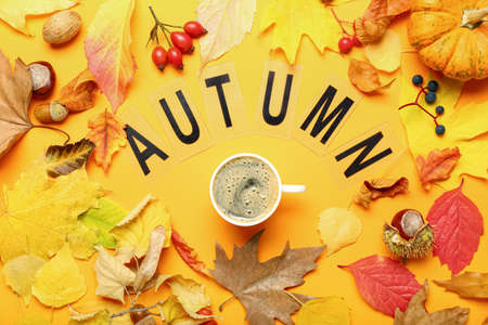 Composition with cup of coffee, word AUTUMN and leaves on yellow backgroundの写真素材