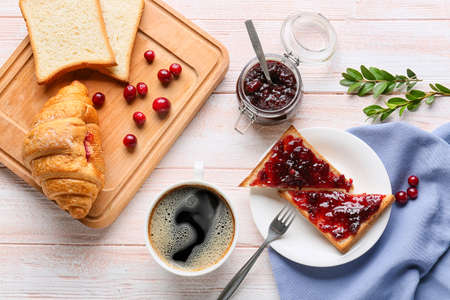 Toasts with tasty lingonberry jam, cup of coffee and croissant on light wooden backgroundの写真素材