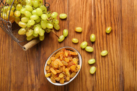 Bowl with tasty raisins and ripe grapes in basket on wooden backgroundの写真素材