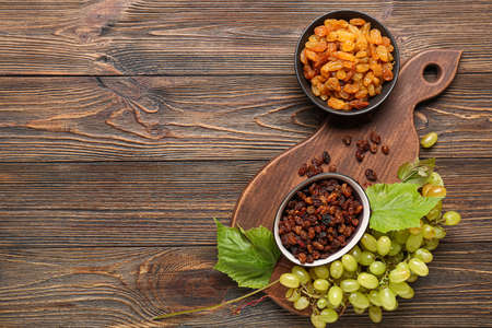 Bowls with tasty raisins and ripe grapes on wooden backgroundの写真素材