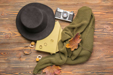 Stylish female accessories, photo camera, notebooks and dry leaves on wooden background