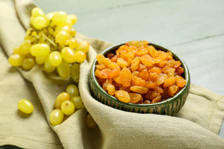 Bowl with tasty raisins and ripe grapes on table, closeup