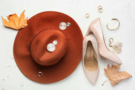 Felt hat, shoes, jewelry and dry leaves on light background