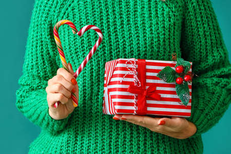 Woman with Christmas gift and candy canes on green background, closeup