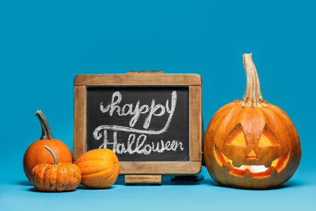 Chalkboard with text HAPPY HALLOWEEN, carved and whole pumpkins on blue backgroundの写真素材