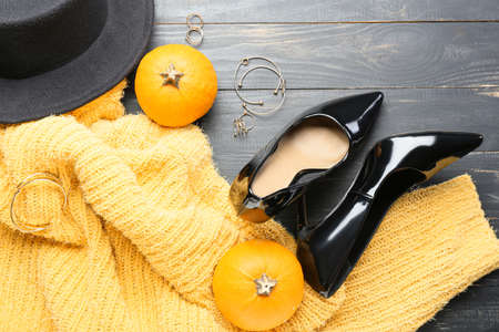 Stylish sweater, pumpkin and female accessories on dark wooden background