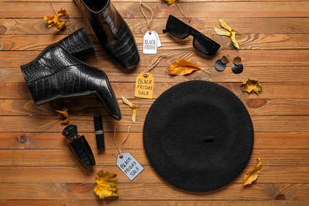 Stylish female accessories, dry leaves and tags with text BLACK FRIDAY SALE on wooden backgroundの写真素材