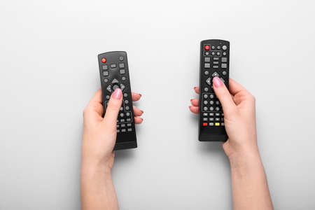 Female hands with TV remote controllers on gray background