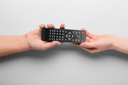 Female hands with TV remote controller on gray backgroundの写真素材