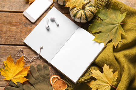 Blank book, mobile phone, earphones and autumn decor on wooden backgroundの写真素材