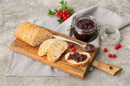 Wooden board of tasty toasts with lingonberry jam on gray background