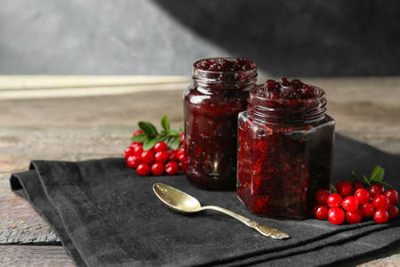Jars of tasty lingonberry jam on table