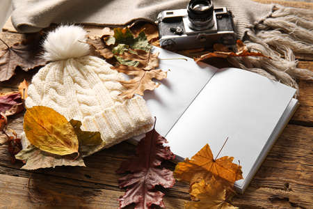 Blank book, warm hat, photo camera and autumn decor on wooden backgroundの写真素材