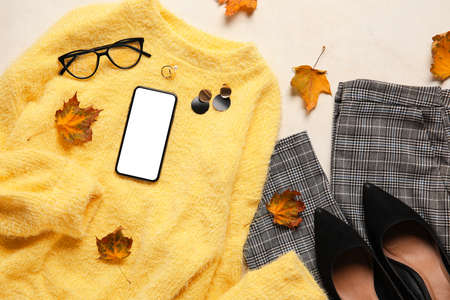 Stylish female accessories, clothes, dry leaves and mobile phone on light background. black friday saleの写真素材