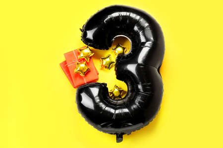 Black balloon in shape of figure 3 and gift boxes on yellow backgroundの写真素材