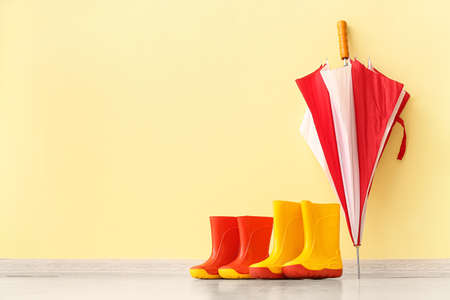 Rubber rain boots and umbrella on floor near color wallの写真素材