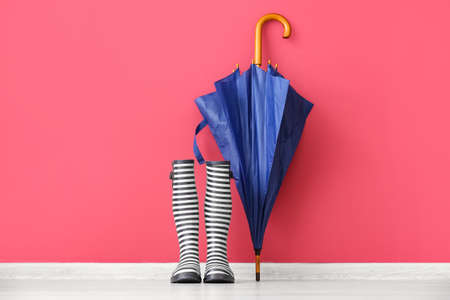 Pair of rubber rain boots and umbrella on floor near color wallの写真素材
