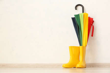 Pair of rubber boots and umbrella against light wallの写真素材