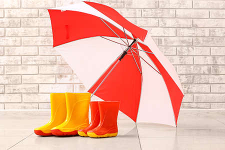 Rubber boots and umbrella on floor near brick wallの写真素材