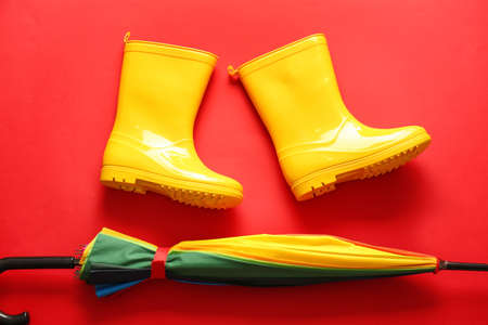 Pair of rubber boots and umbrella on red backgroundの写真素材